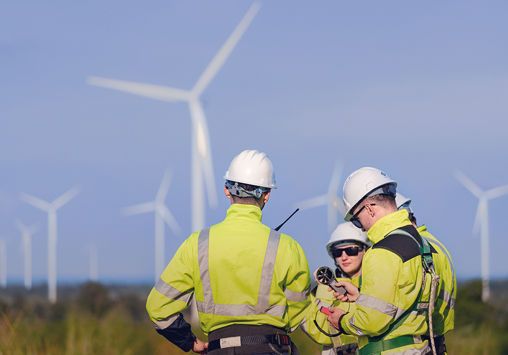 Un equipo de ingenieros con equipos de seguridad de alta visibilidad se reúnen en un parque eólico, realizando inspecciones y discutiendo proyectos de energía renovable